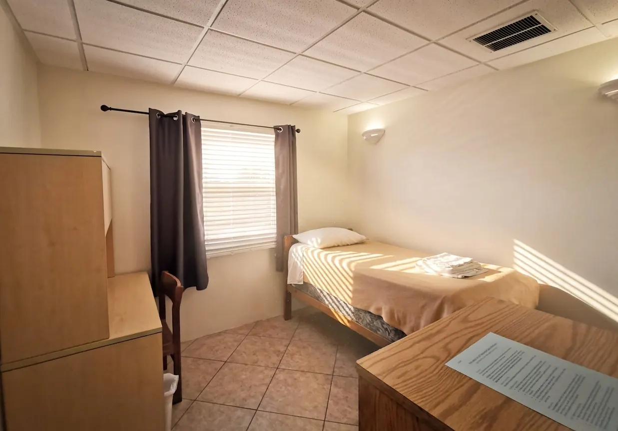 Una habitación con la cama hecha, una ventana con cortinas y un escritorio junto a la pared