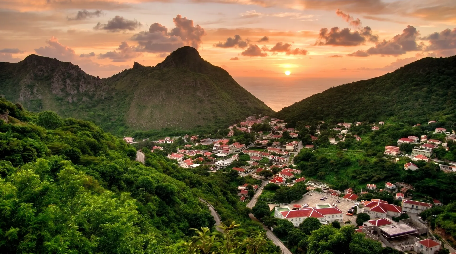 Sunset over Saba, red-roofed houses filling the green valley between the peaks, with the sea beyond