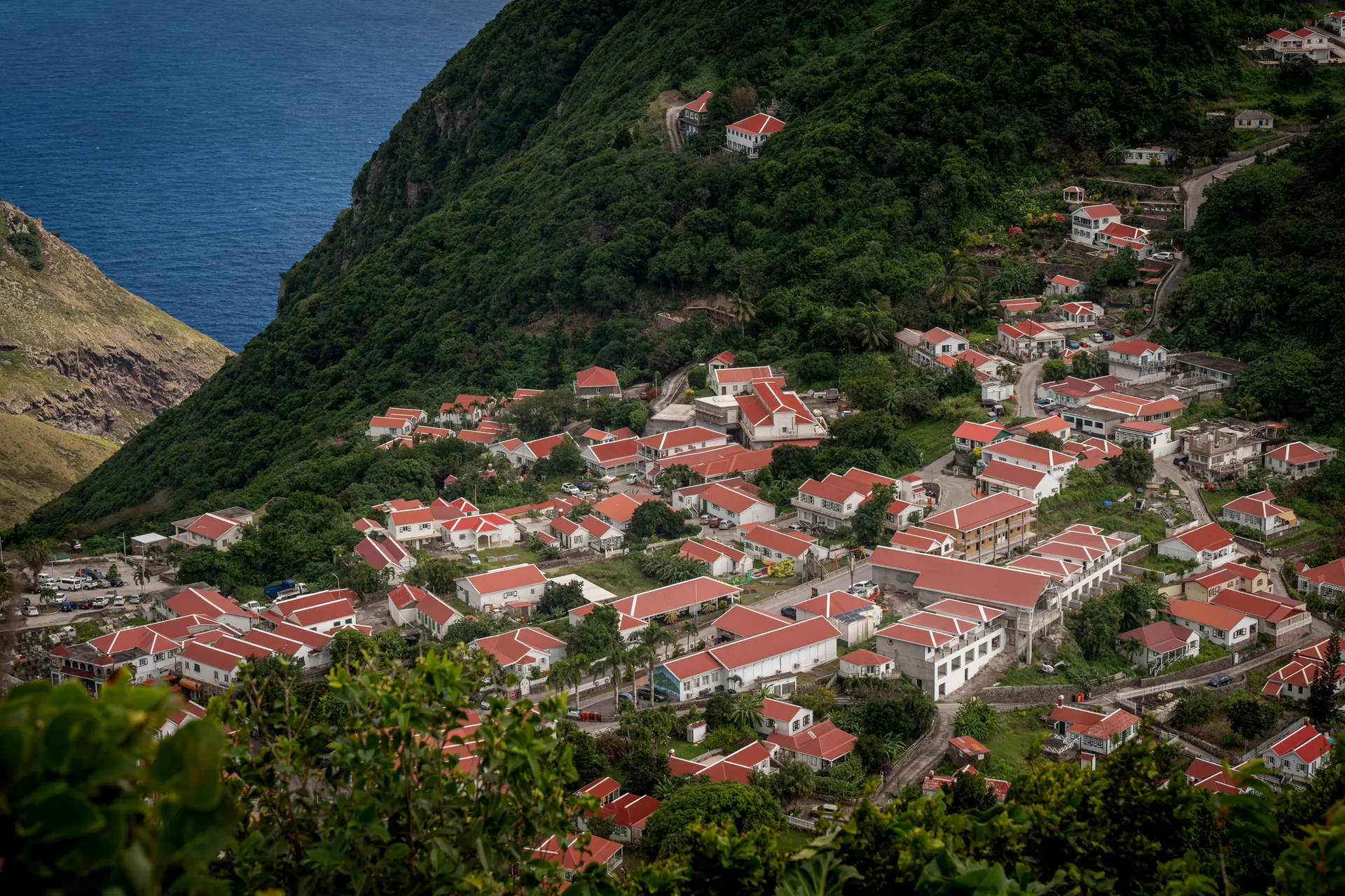 Atardecer sobre Saba, casas de techos rojos llenando el valle verde entre los picos, con el mar al fondo